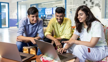 Three software engineers sitting on couch and collaborating in front of a laptop.